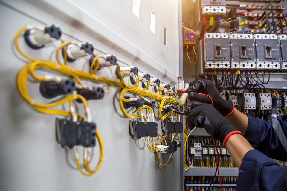 Technicien électricien travaillant sur tableau électrique industriel, portant gants de protection noirs avec liserés rouges
