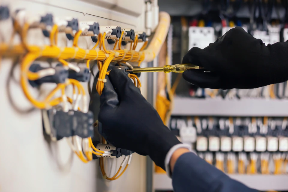 Technicien en combinaison travaillant sur panneau électrique industriel, manipulation de câbles avec outil de précision
